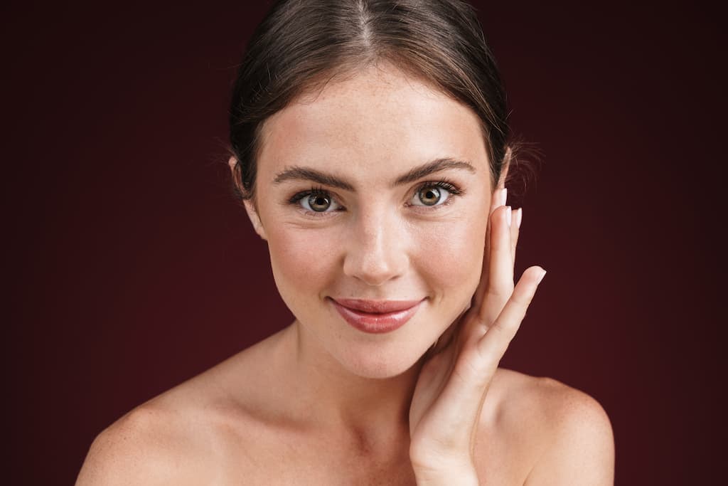 Woman with smooth, radiant skin and even complexion touching her face gently, demonstrating the improved skin texture and luminous results achievable with MOXI laser treatment