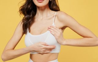 A woman in a white sports bra against a yellow background, showcasing the improved shape, firmness, and elevated nipple position of a natural-looking breast lift.